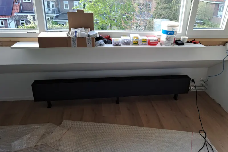 Zwarte convectorradiator onder een raam, tijdens de werkzaamheden